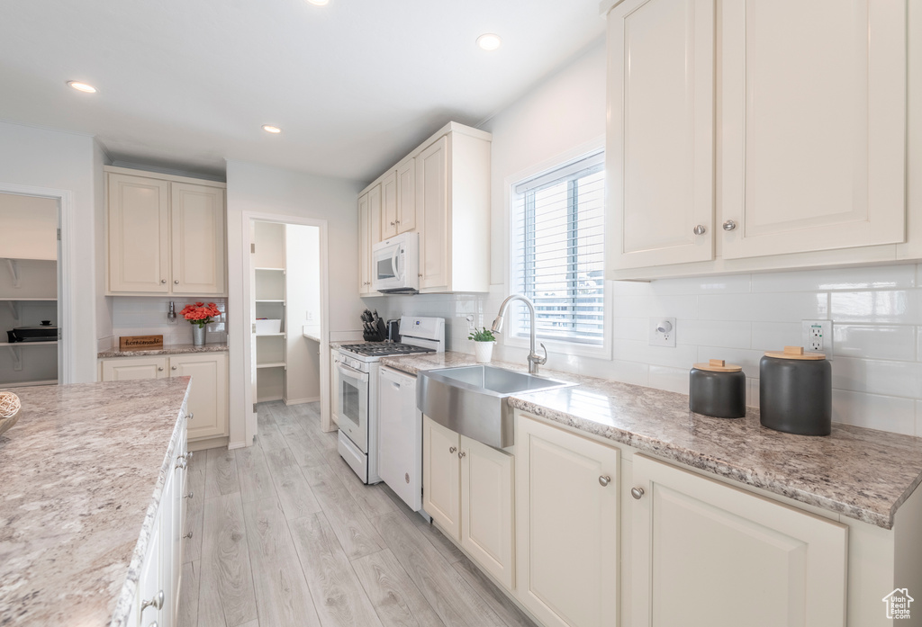 Kitchen featuring sink, light stone counters, white appliances, light wood-type flooring, and decorative backsplash