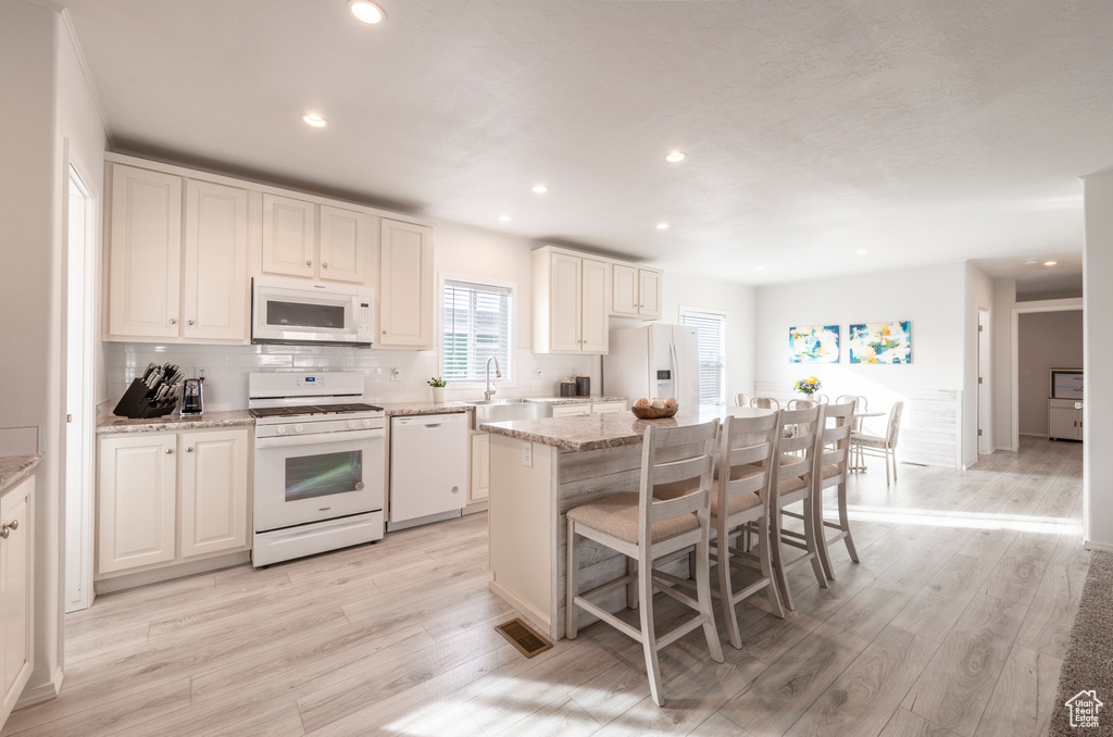 Kitchen featuring white cabinetry, light stone countertops, white appliances, a center island, and light wood-type flooring