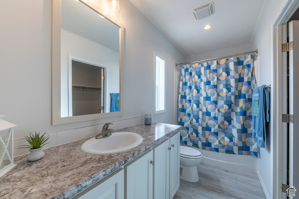 Full bathroom with toilet, wood-type flooring, vanity, and shower / tub combo