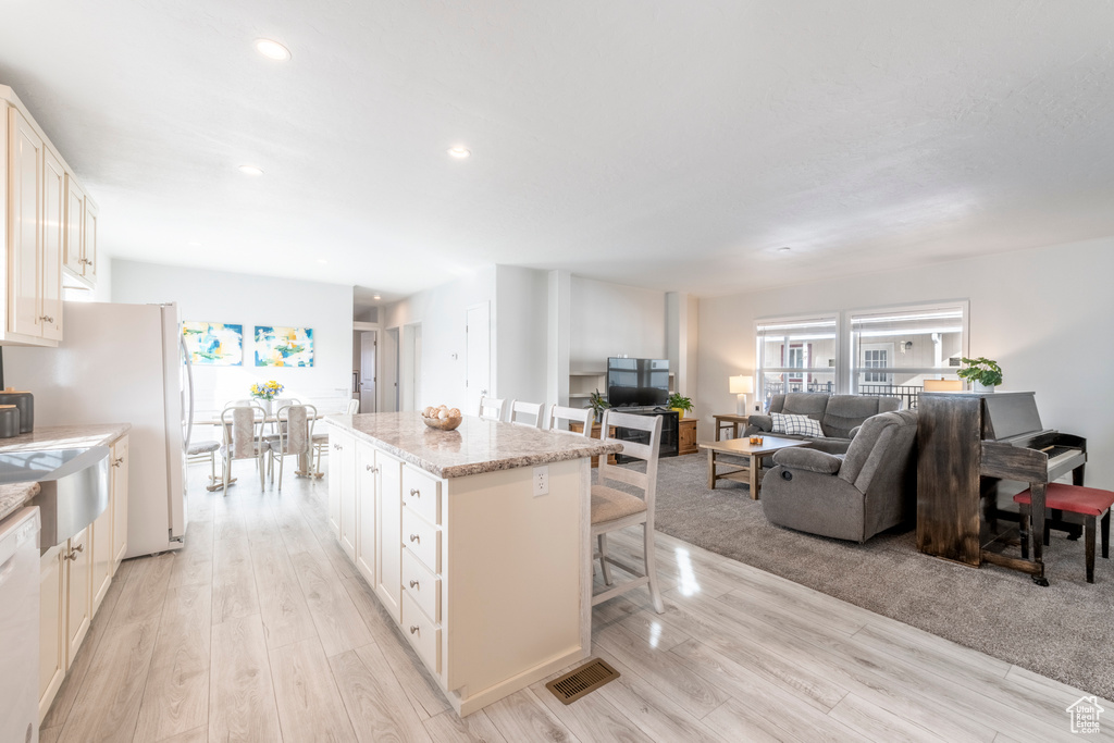 Kitchen featuring light hardwood / wood-style floors, a center island, white cabinets, a breakfast bar area, and light stone countertops