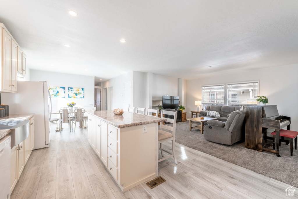 Kitchen featuring light hardwood / wood-style floors, white cabinets, a kitchen breakfast bar, a kitchen island, and light stone countertops