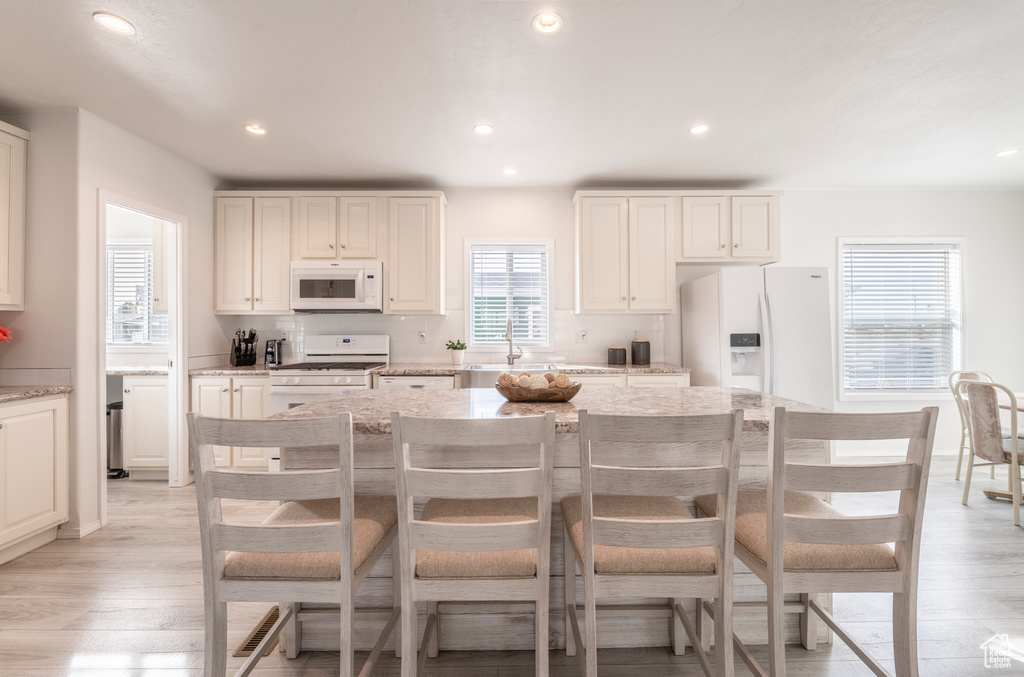 Kitchen featuring a kitchen island, light stone countertops, white appliances, and light hardwood / wood-style flooring