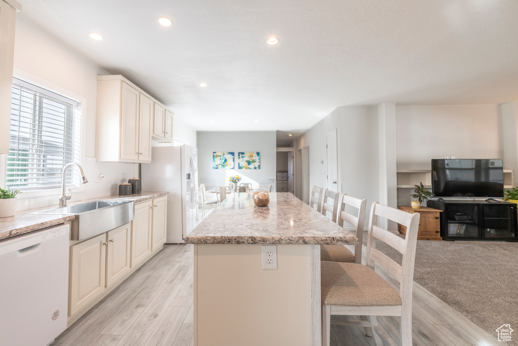 Kitchen featuring sink, light stone countertops, a kitchen bar, white appliances, and a center island