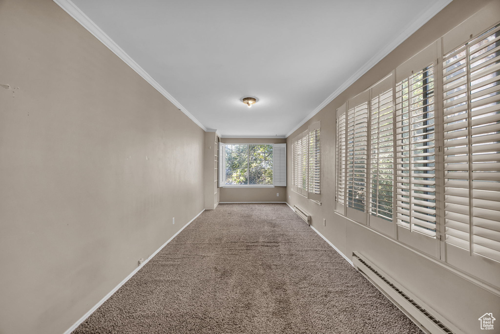 Hall featuring a baseboard heating unit, light colored carpet, ornamental molding, and plenty of natural light