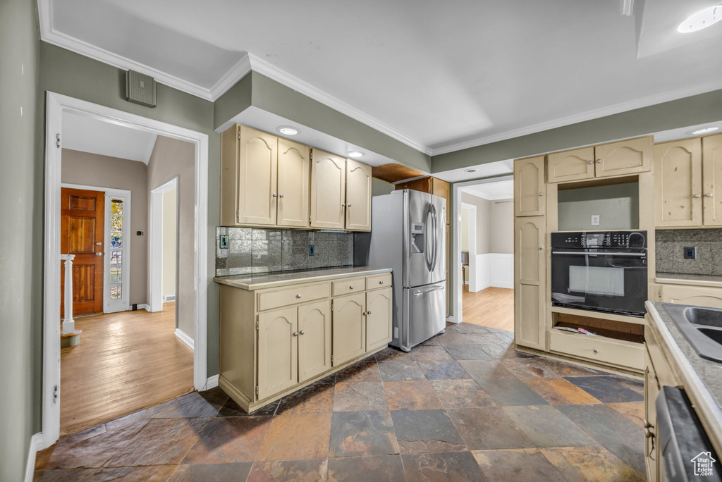 Kitchen with dark hardwood / wood-style floors, decorative backsplash, cream cabinets, and appliances with stainless steel finishes