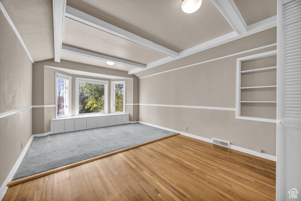 Unfurnished room featuring hardwood / wood-style floors, radiator heating unit, and vaulted ceiling with beams