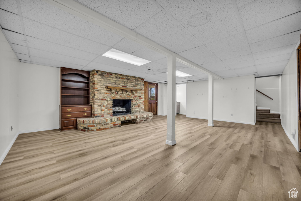 Basement with light wood-type flooring, a paneled ceiling, and a fireplace