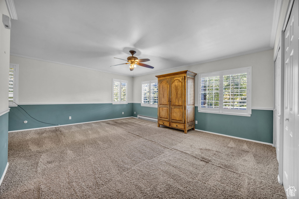 Interior space with a baseboard heating unit, light colored carpet, and crown molding