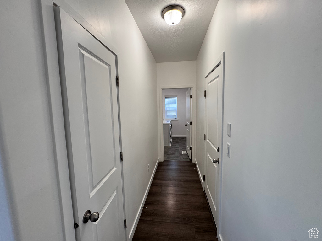 Corridor with dark wood finished floors, baseboards, and a textured ceiling