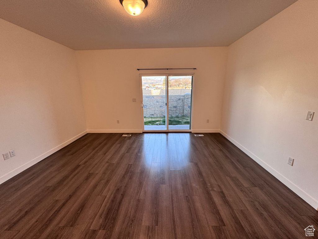 Spare room with baseboards, dark wood-type flooring, and a textured ceiling