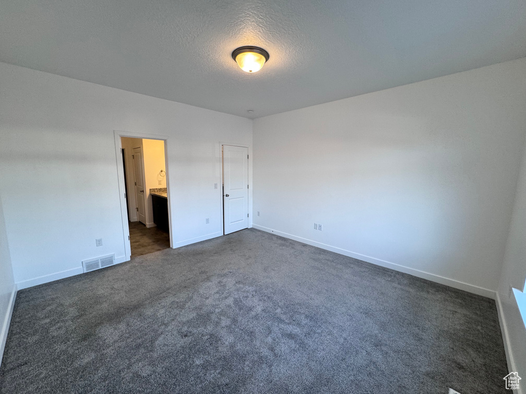 Unfurnished bedroom featuring dark carpet, baseboards, a textured ceiling, and visible vents