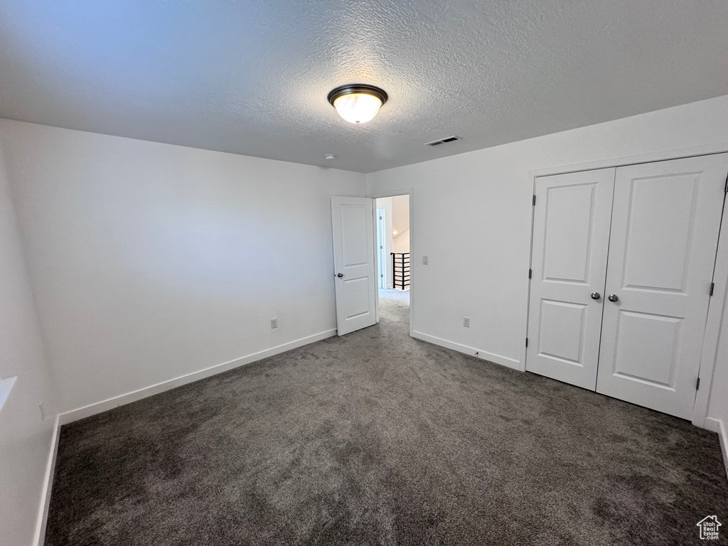 Unfurnished bedroom with a closet, a textured ceiling, visible vents, baseboards, and carpet floors
