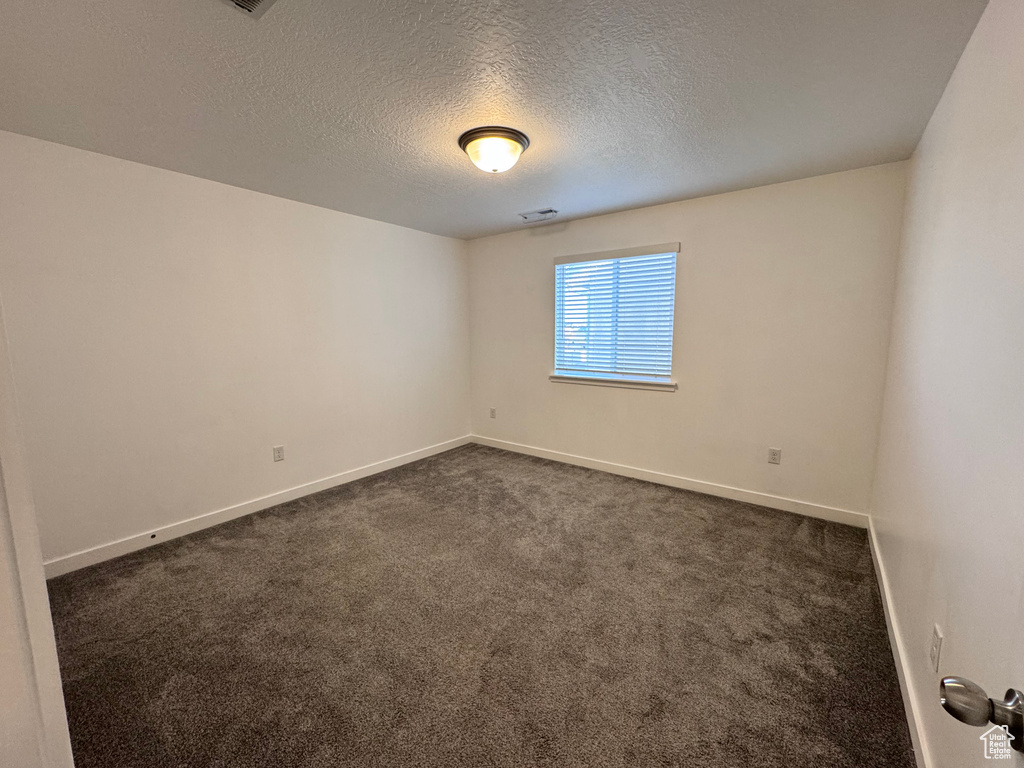 Empty room with baseboards, dark carpet, and a textured ceiling