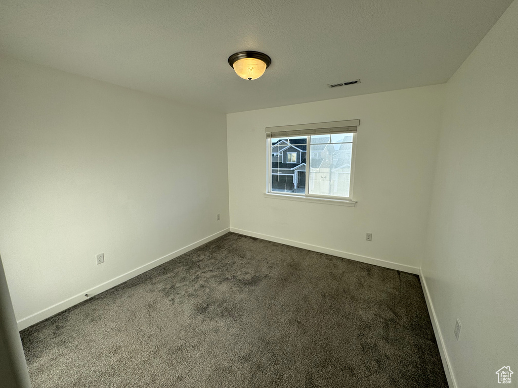 Empty room featuring baseboards, visible vents, and dark colored carpet
