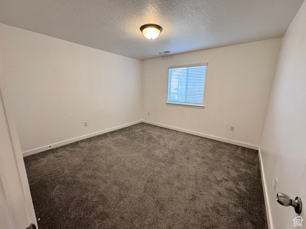 Unfurnished room with baseboards, a textured ceiling, visible vents, and dark colored carpet