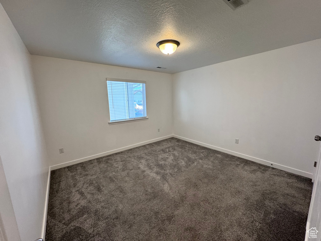 Unfurnished room featuring baseboards, dark colored carpet, and a textured ceiling