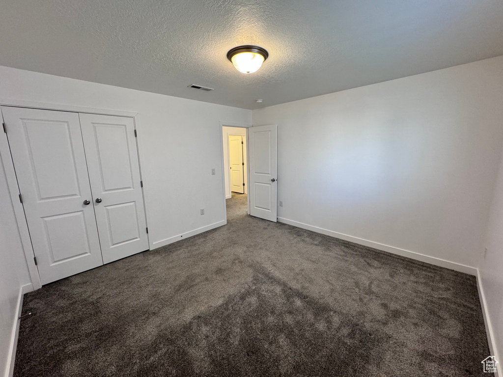 Unfurnished bedroom with a closet, a textured ceiling, dark colored carpet, baseboards, and visible vents