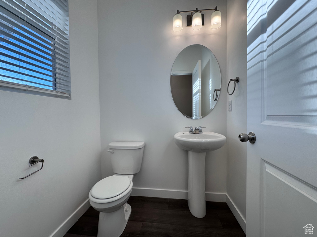 Half bath with baseboards, wood finished floors, toilet, and a sink