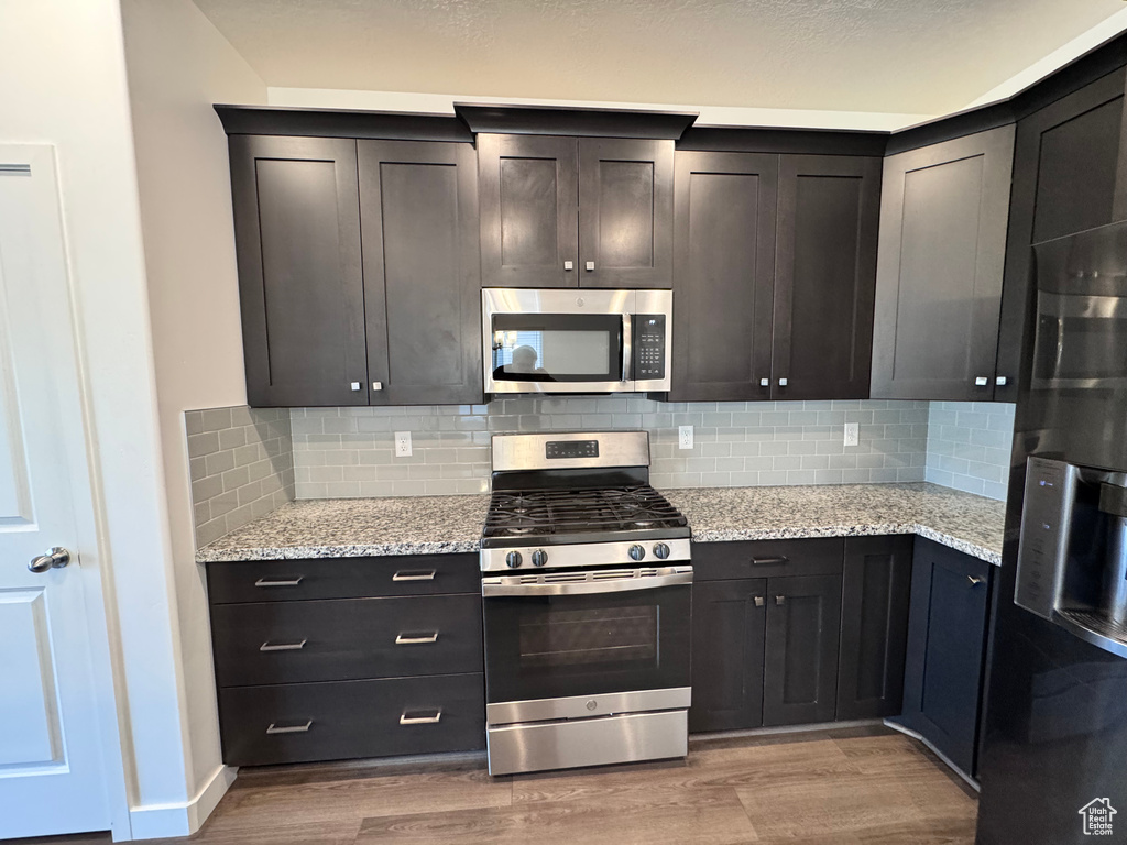Kitchen with light stone countertops, light wood-style flooring, stainless steel appliances, and backsplash