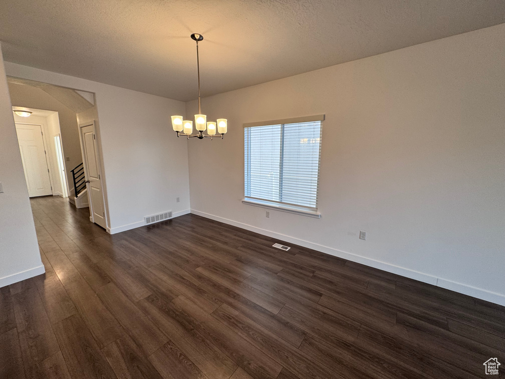 Unfurnished room with dark wood-style floors, visible vents, baseboards, and a chandelier