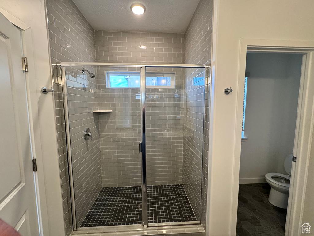 Bathroom with a textured ceiling, toilet, and a stall shower