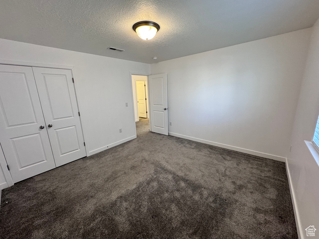 Unfurnished bedroom with baseboards, a textured ceiling, dark carpet, visible vents, and a closet