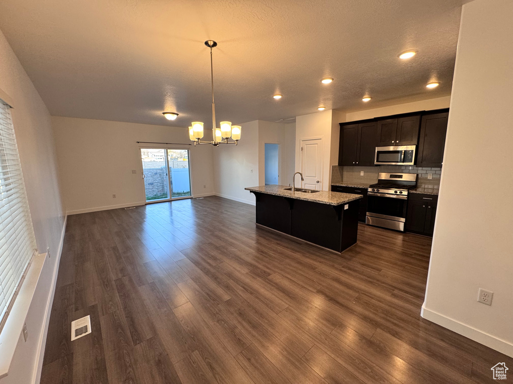 Kitchen featuring open floor plan, an inviting chandelier, stainless steel appliances, backsplash, and dark wood-style floors
