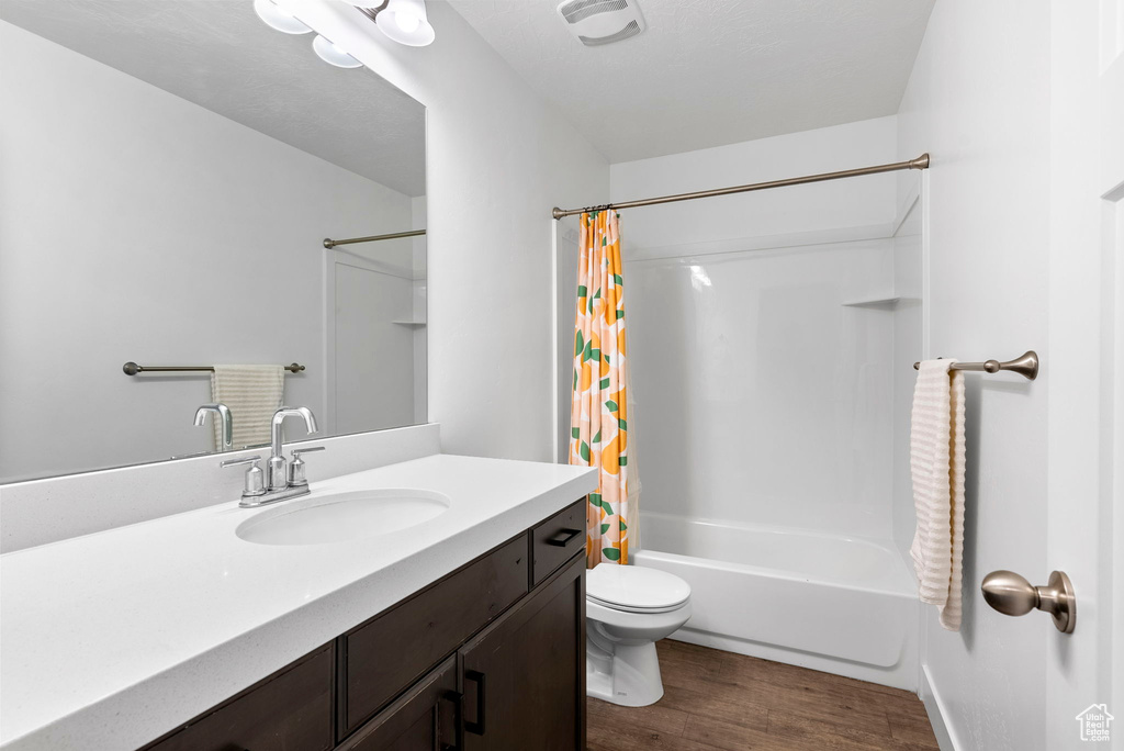 Full bathroom with hardwood / wood-style floors, shower / bath combo, vanity, and toilet