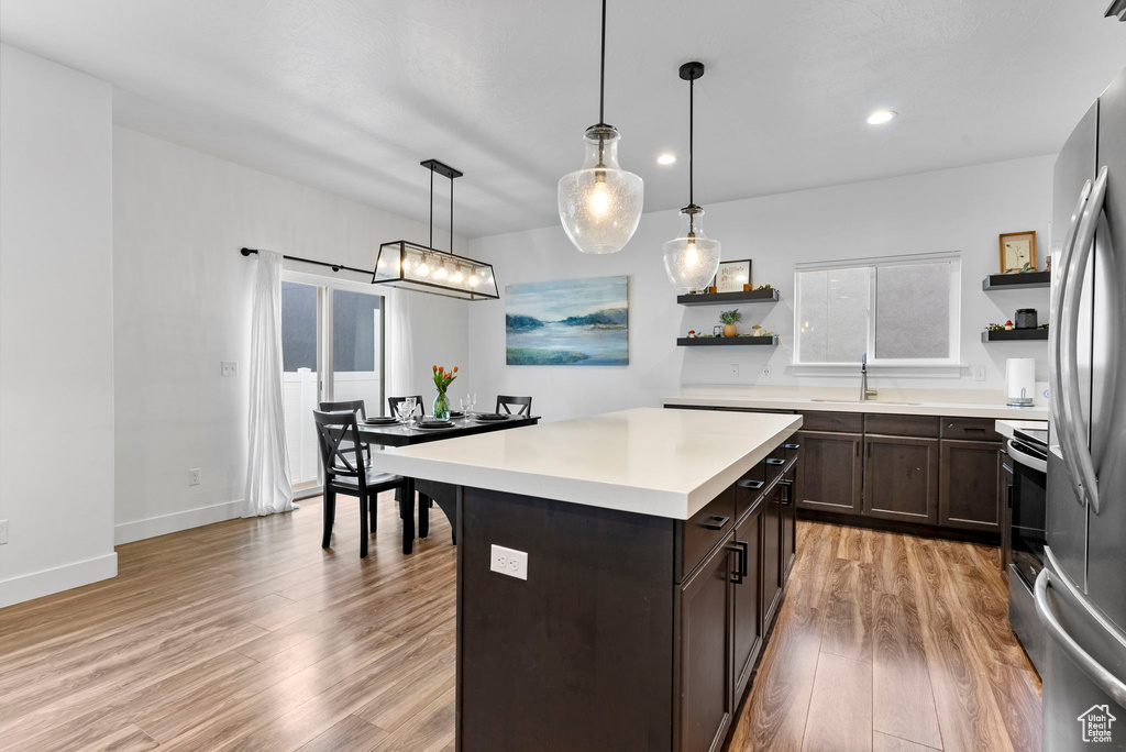 Kitchen with a center island, dark brown cabinetry, hanging light fixtures, light wood-type flooring, and appliances with stainless steel finishes