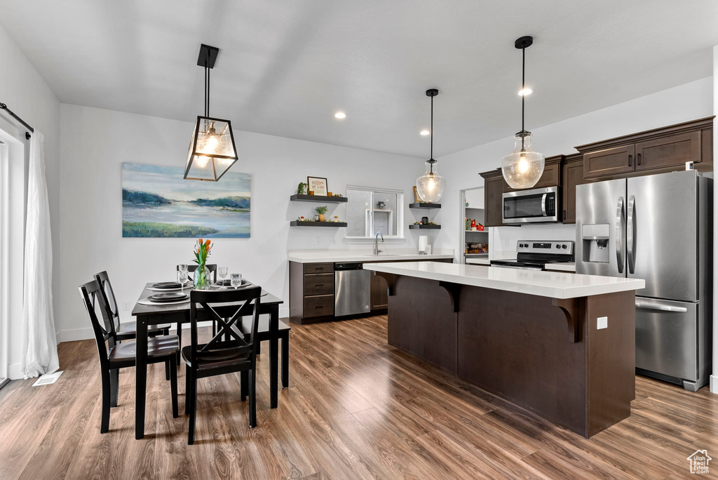 Kitchen with dark brown cabinets, stainless steel appliances, pendant lighting, and dark hardwood / wood-style flooring