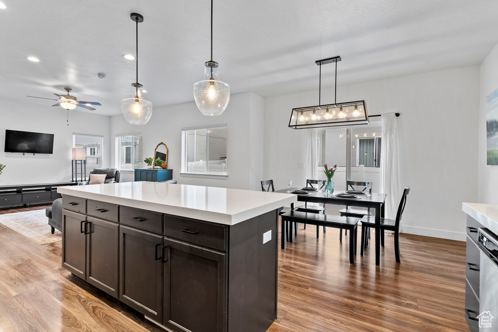 Kitchen with dark brown cabinetry, ceiling fan, decorative light fixtures, light hardwood / wood-style flooring, and a kitchen island