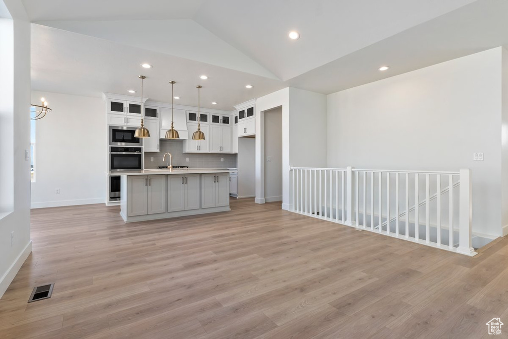 Kitchen with stainless steel appliances, hanging light fixtures, vaulted ceiling, an island with sink, and light hardwood / wood-style flooring