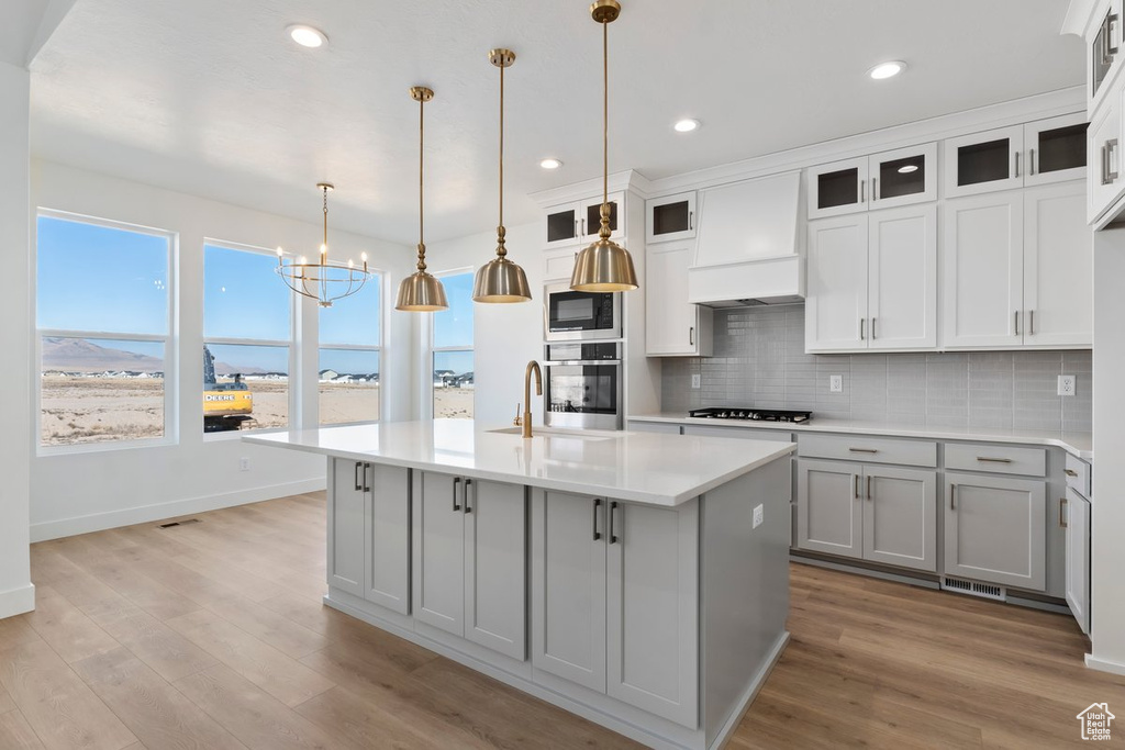 Kitchen with an island with sink, gray cabinets, hanging light fixtures, and appliances with stainless steel finishes