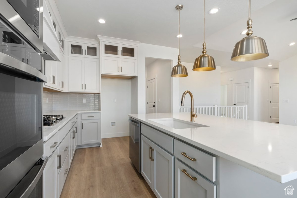 Kitchen with stainless steel appliances, hanging light fixtures, sink, white cabinets, and a kitchen island with sink