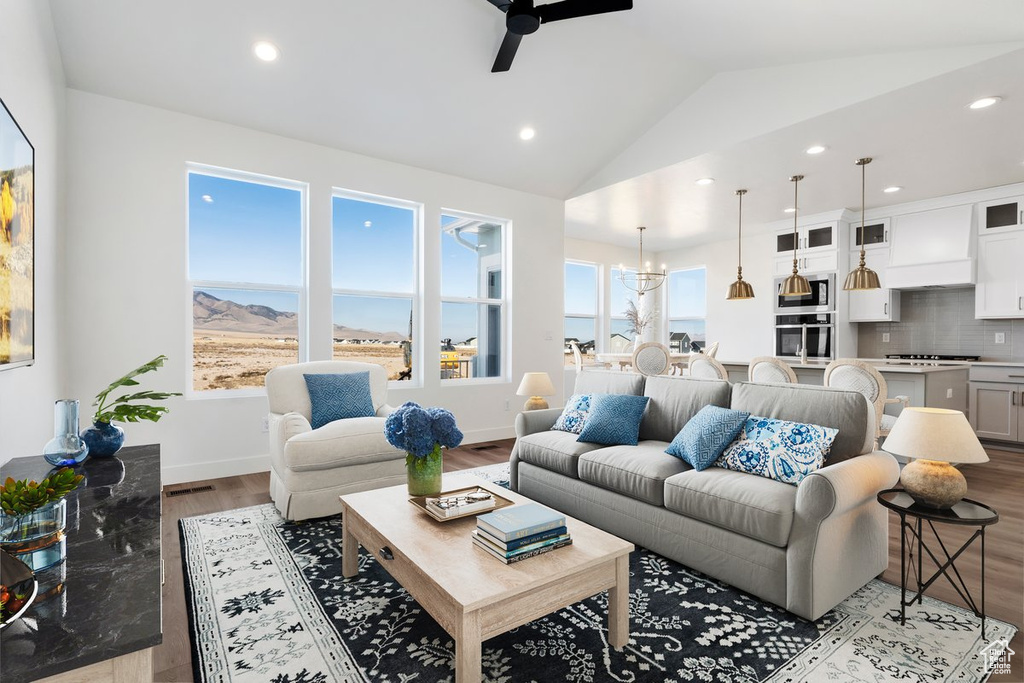 Living room featuring ceiling fan with notable chandelier, light hardwood / wood-style floors, and lofted ceiling