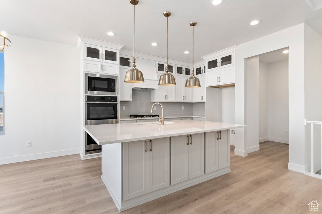 Kitchen with pendant lighting, appliances with stainless steel finishes, a center island with sink, and tasteful backsplash