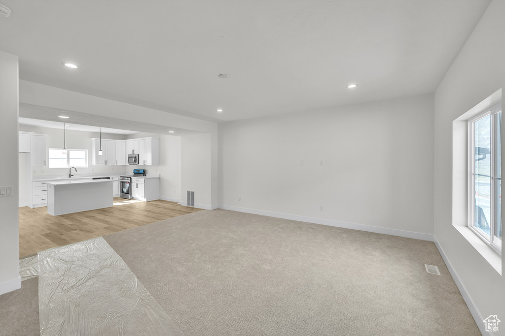 Unfurnished living room featuring recessed lighting, visible vents, a sink, baseboards, and light colored carpet