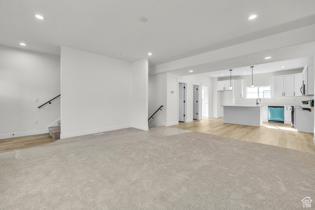 Unfurnished living room featuring a sink, baseboards, recessed lighting, light wood-style floors, and light colored carpet