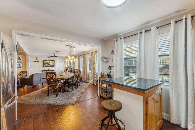 Kitchen with stainless steel refrigerator, ceiling fan, a breakfast bar area, decorative light fixtures, and dark wood-type flooring