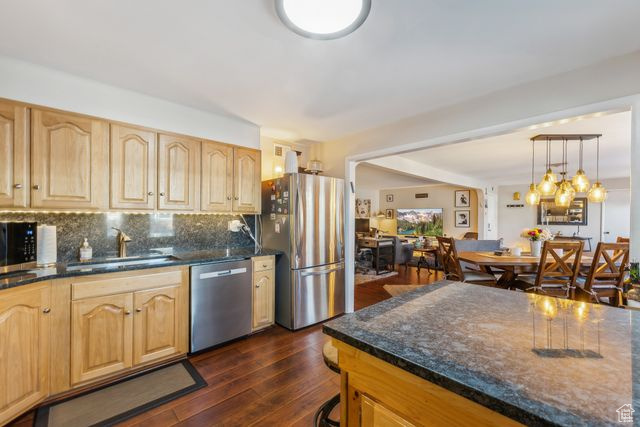 Kitchen with light brown cabinets, dark hardwood / wood-style flooring, appliances with stainless steel finishes, and tasteful backsplash