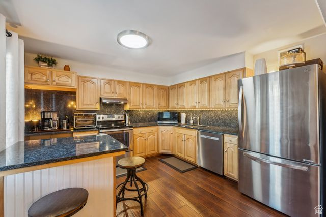 Kitchen with appliances with stainless steel finishes, a kitchen breakfast bar, light brown cabinetry, a kitchen island, and dark hardwood / wood-style flooring