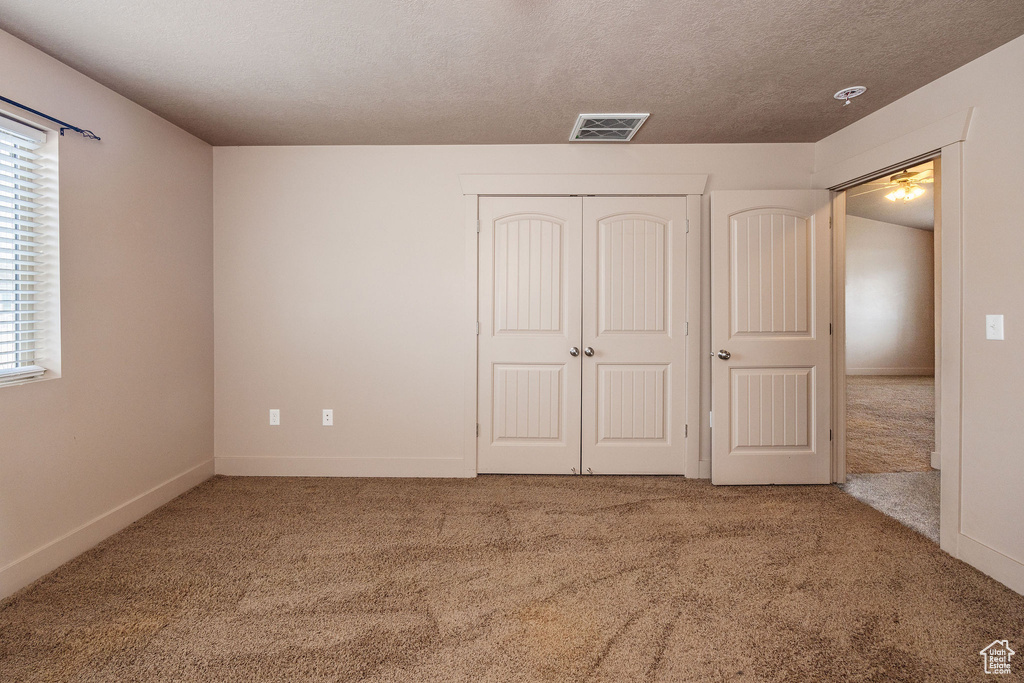 Unfurnished bedroom with carpet flooring, multiple windows, a closet, and a textured ceiling
