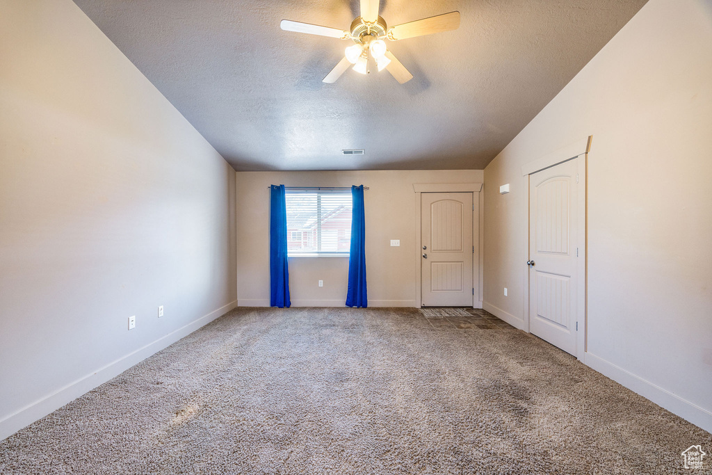 Carpeted spare room featuring ceiling fan, a textured ceiling, and vaulted ceiling