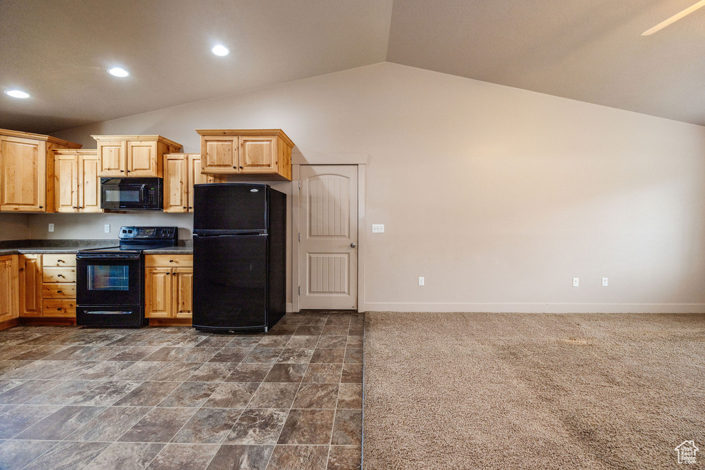 Kitchen with light brown cabinetry, black appliances, lofted ceiling, and dark carpet