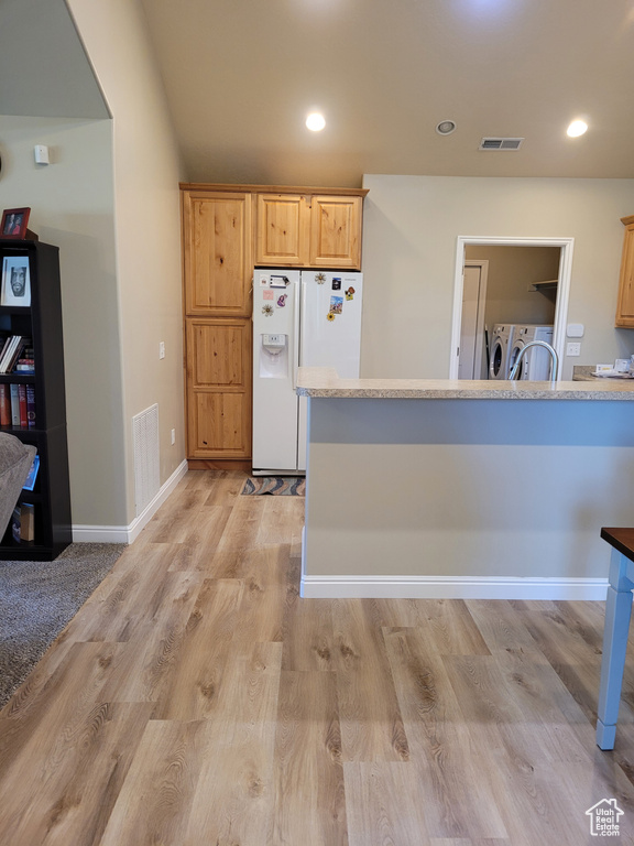 Kitchen featuring light brown cabinets, light hardwood / wood-style floors, white refrigerator with ice dispenser, and washer and dryer