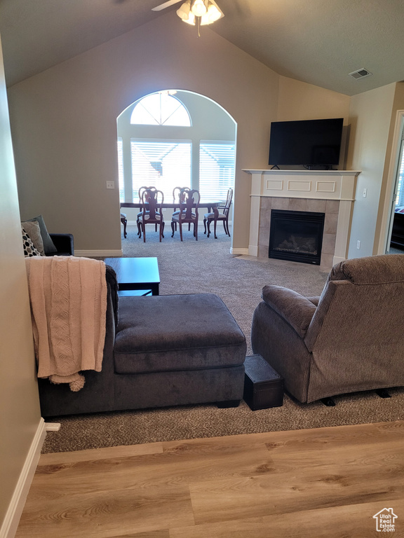Living room featuring a tiled fireplace, light hardwood / wood-style flooring, lofted ceiling, and ceiling fan