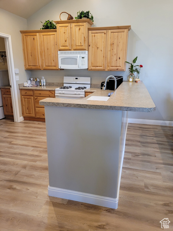 Kitchen with light brown cabinets, kitchen peninsula, white appliances, and light hardwood / wood-style floors