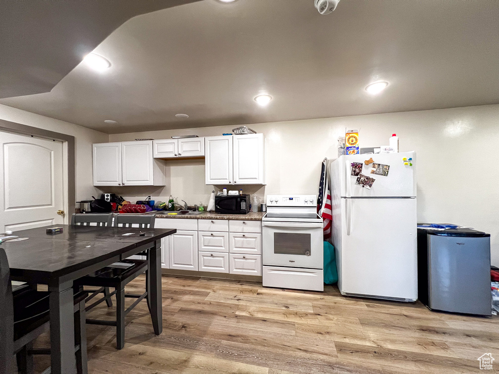 Kitchen with white cabinets, light wood-type flooring, and white appliances