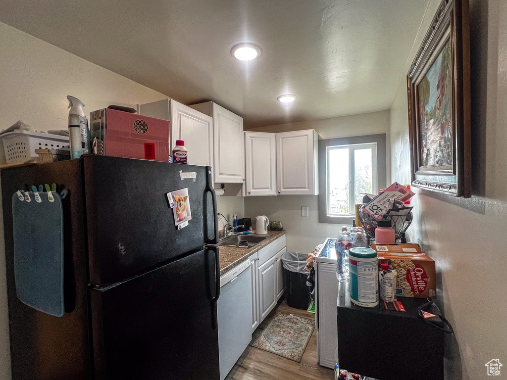 Kitchen featuring white cabinetry, light hardwood / wood-style floors, white dishwasher, and black refrigerator