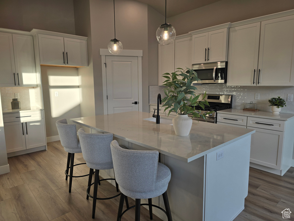 Kitchen with pendant lighting, stainless steel appliances, white cabinetry, and a kitchen island with sink